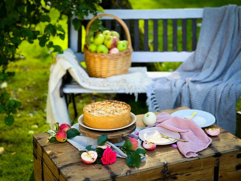A rustic outdoor picnic setting with apple pie and basket of apples, showcasing summer vibes.