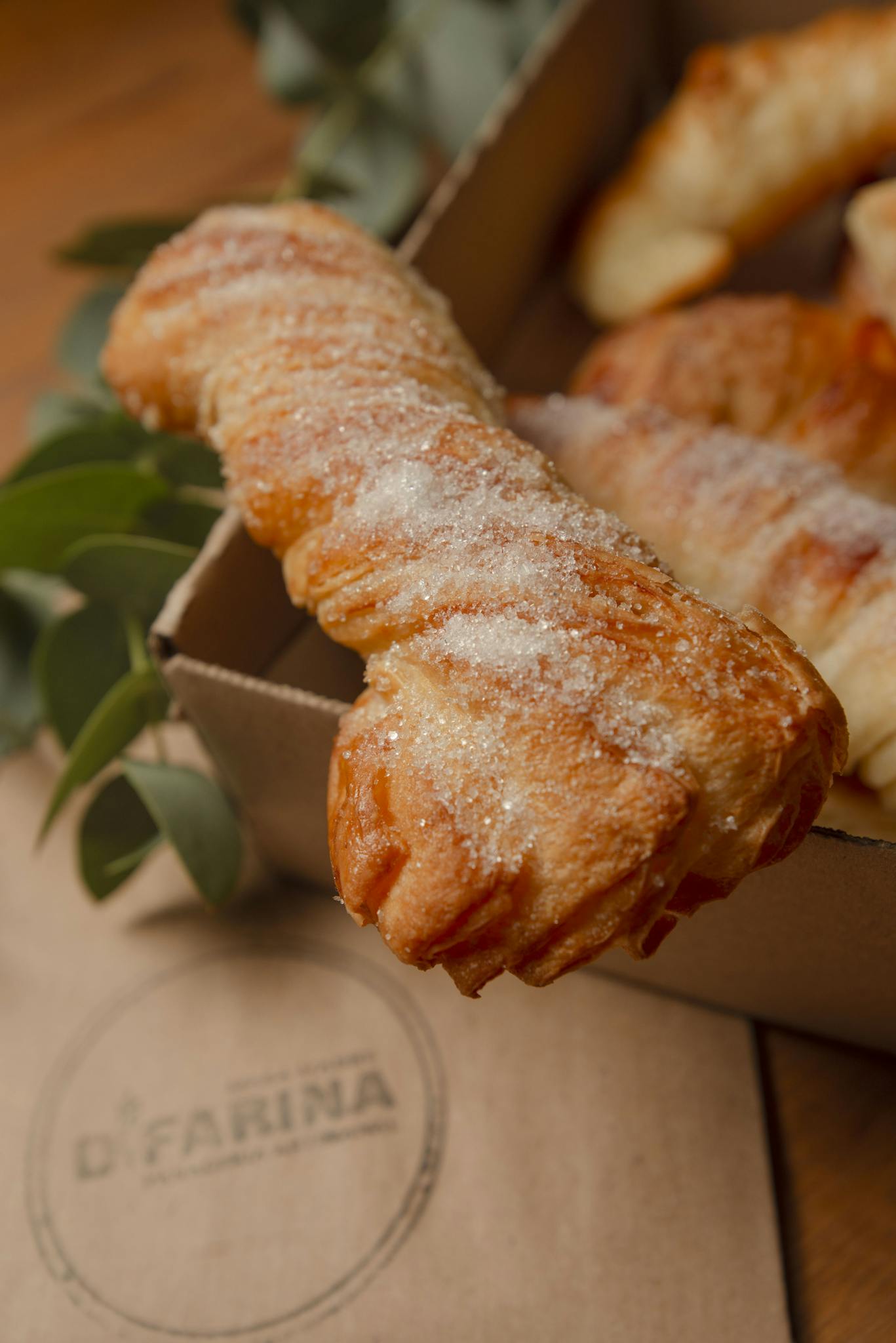 Delicious sugary pastries in a cardboard box, surrounded by green leaves, perfect for a cozy dessert setting.